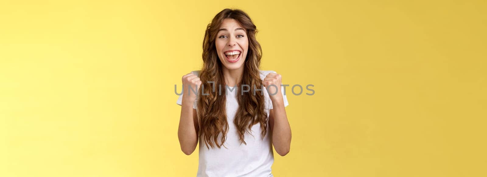 Yes finally success. Cheerful enthusiastic happy girl pump fists lift hands victory joy celebration gesture smiling broadly relieved winning lottery amused stand yellow background triumphing.