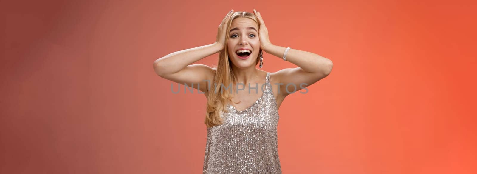Amazed excited nervous young beautiful blond woman in silver stylish dress cannot believe own luck happiness hold hands head smiling screaming astonished positive awesome news, triumphing.