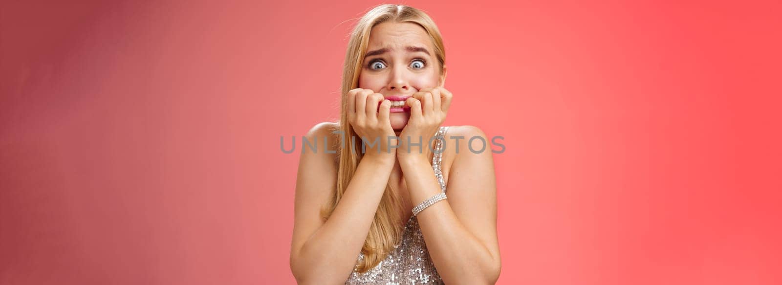 Frightened afraid panicking young cute blond woman biting nails pop eyes scared camera look terrified stunned speechless stare forward standing red background gasping trembling fear.