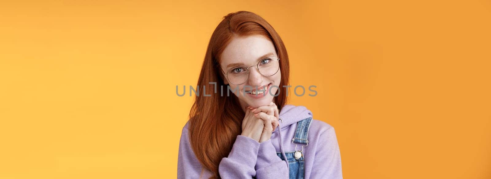 Flirty young clingy girlfriend redhead girl trying learn flirt making creepy lovely smile lean head palms seducing guy standing orange background glancing romantically wear glasses by Benzoix