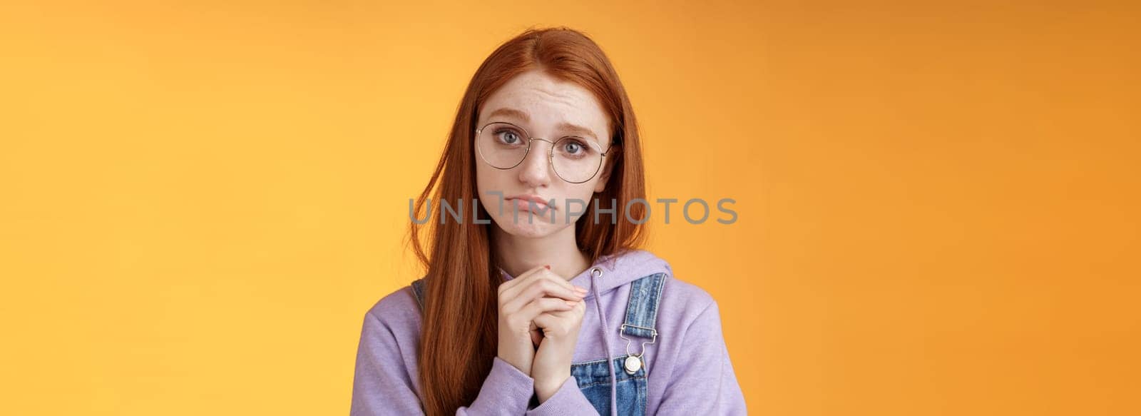 Pretty please. Clingy young sad sulking redhead girl sibling wearing glasses pouting silly press palms begging gesture pleading wanna receive help promise be good ask favour, orange background.