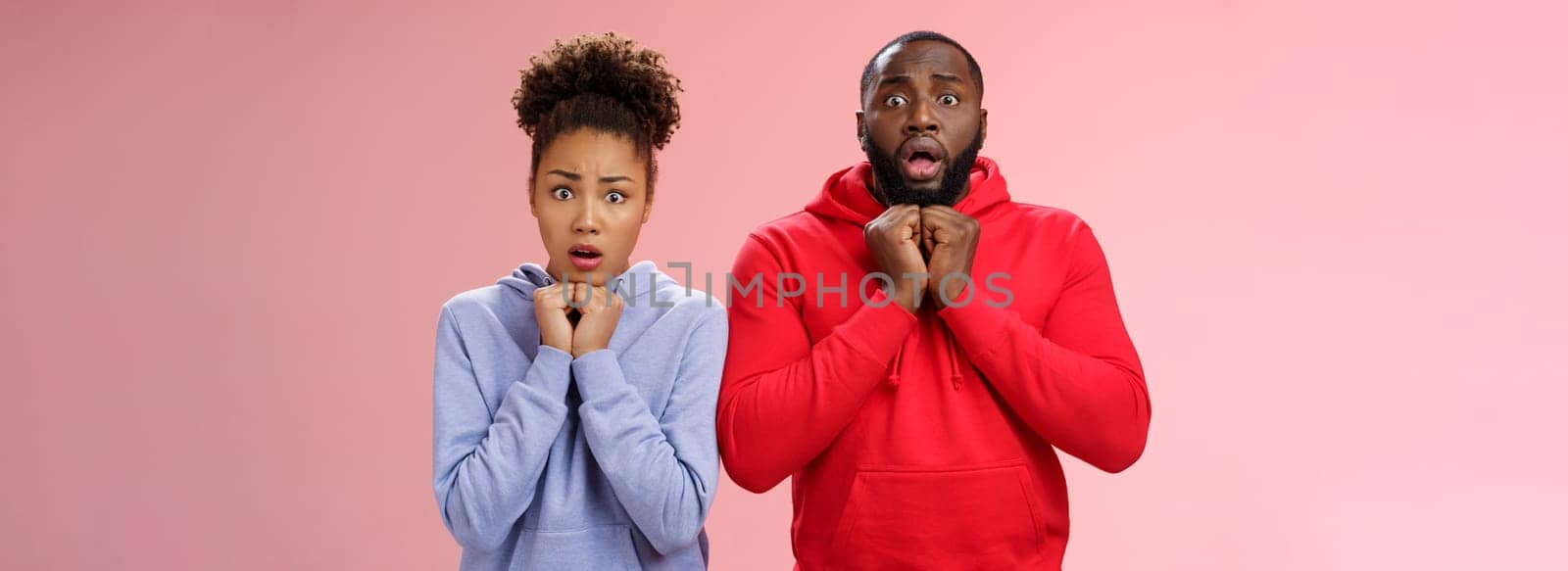 Lifestyle. Upset worried two siblings watching together scary disturbing horror movie gasping frowning cringing shock intense emotions press hands chest widen eyes terrified standing nervous pink background.