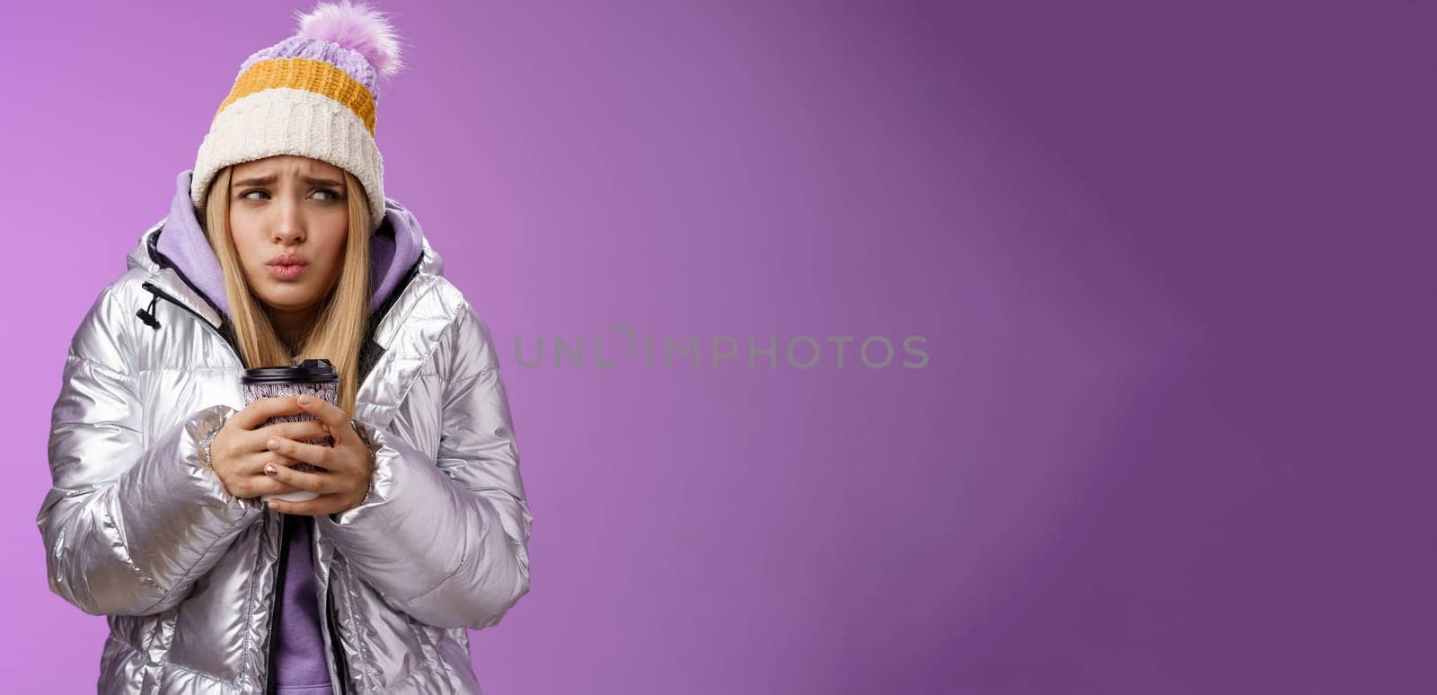 Trembling uncomfortable cute pouting young blond girl feel freezing cold winter snowy weather outside shaking low temperature hold take-away hot coffee cup warming up, purple background by Benzoix