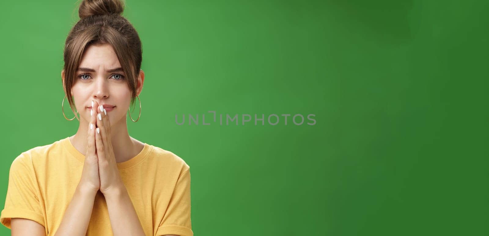 Waist-up shot of nervous upset girlfriend holding hands in pray over lips frowning looking concerned worrying for boyfriend standing anxious and sad over green background. Emotions and body language concept