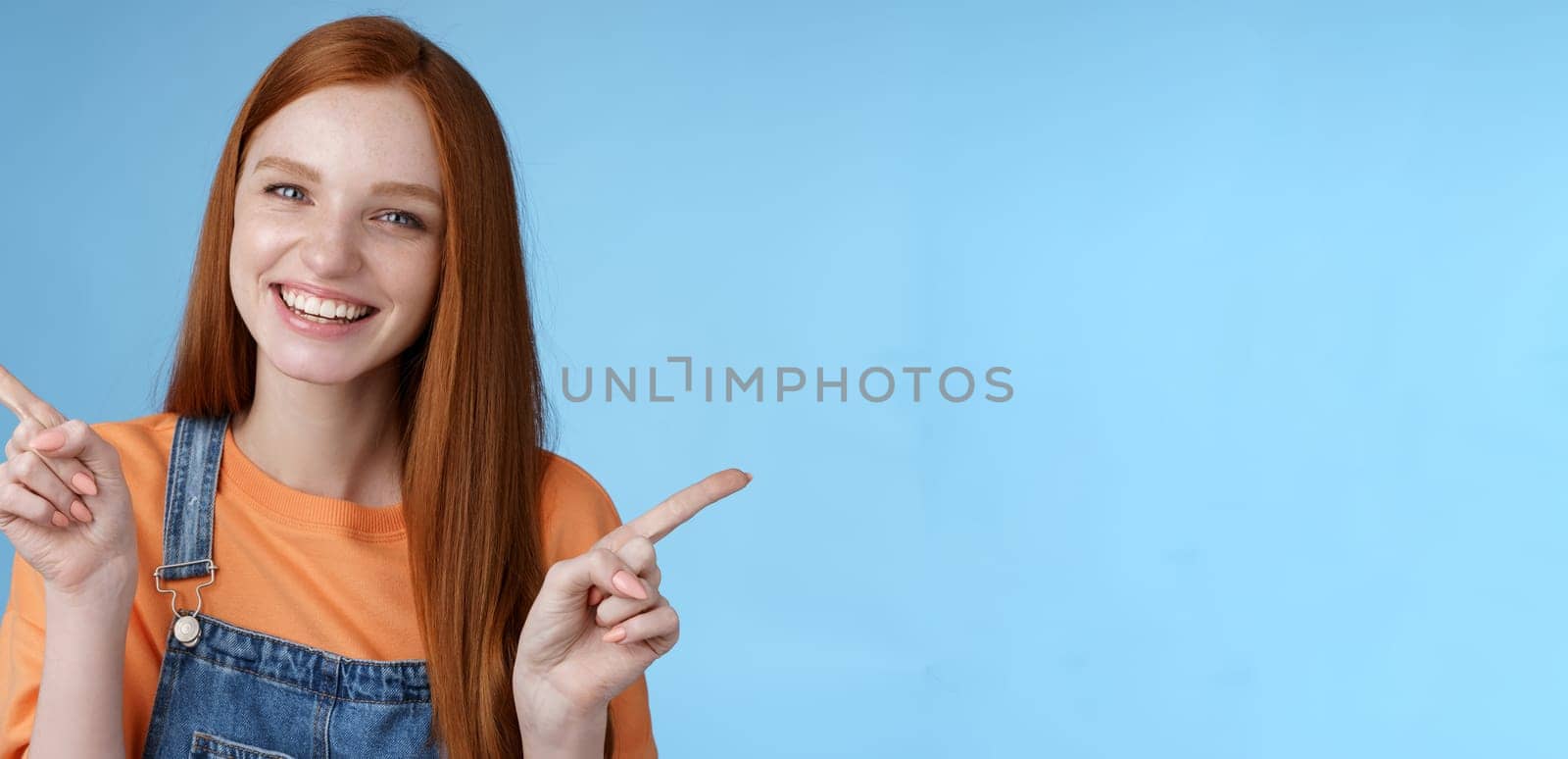 Friendly happy laughing pretty redhead girl female student showing lots opportunities advice make choice pointing sideways left right introducing different product grinning gladly, blue background by Benzoix