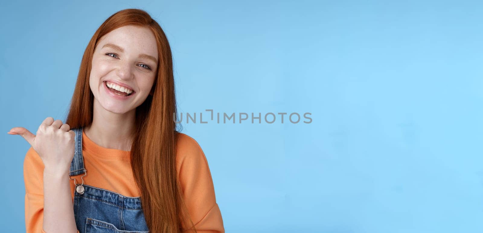 Girl introducing her friend pointing thumb left smiling laughing joyfully proudly telling pros cool product recommend telling about cozy cafe tasty coffee having fun posing blue background by Benzoix