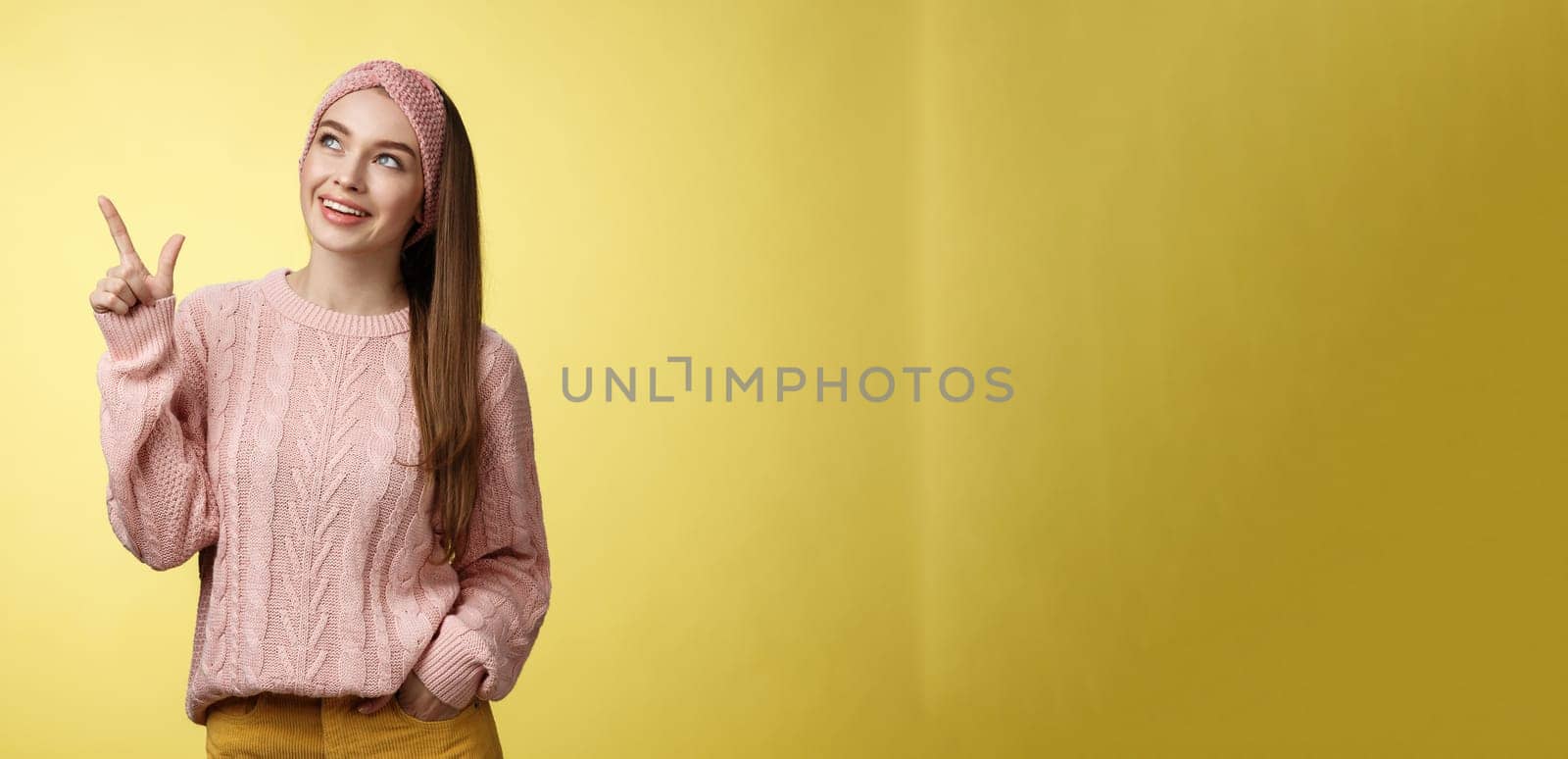 Portrait of amused interested cute 20s european girl wearing sweater, headband looking upper left corner pointing sideways smiling intrigued, ecstatic, captured by curious promo over yellow wall by Benzoix