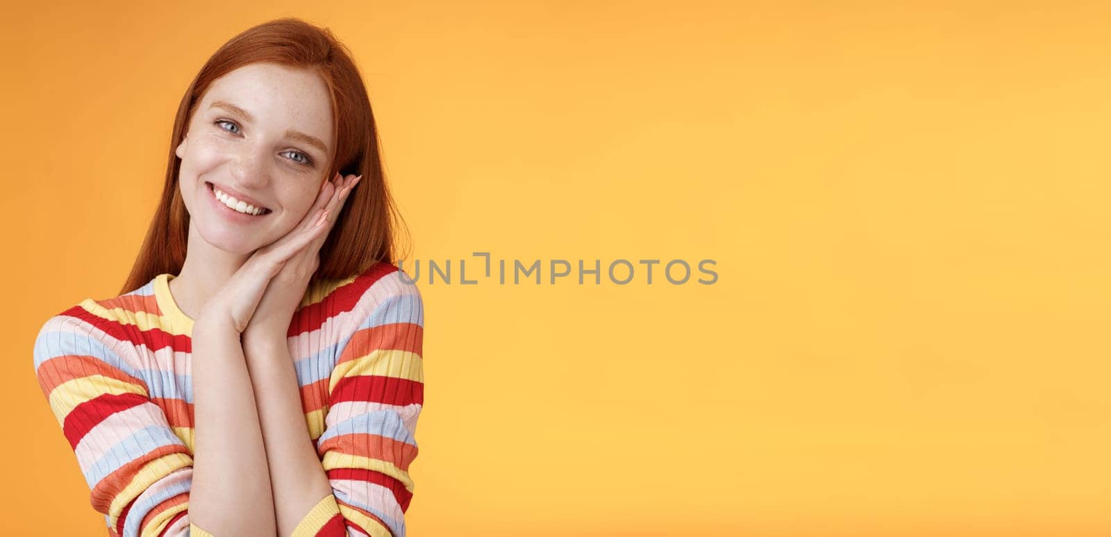 Lovely young flirty redhead european girl smiling broadly excited happy lean palm receive sweet tender present look grateful amused joyfully reacting pleasing moment, standing orange background by Benzoix