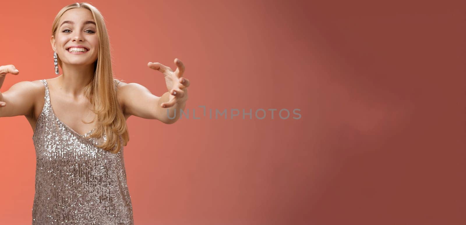 Excited obsessed attractive crazy blond woman in glamour silver dress smiling weird thrilled stretch hands like claws wanna embrace hug ex-boyfriend being clingy, standing red background.