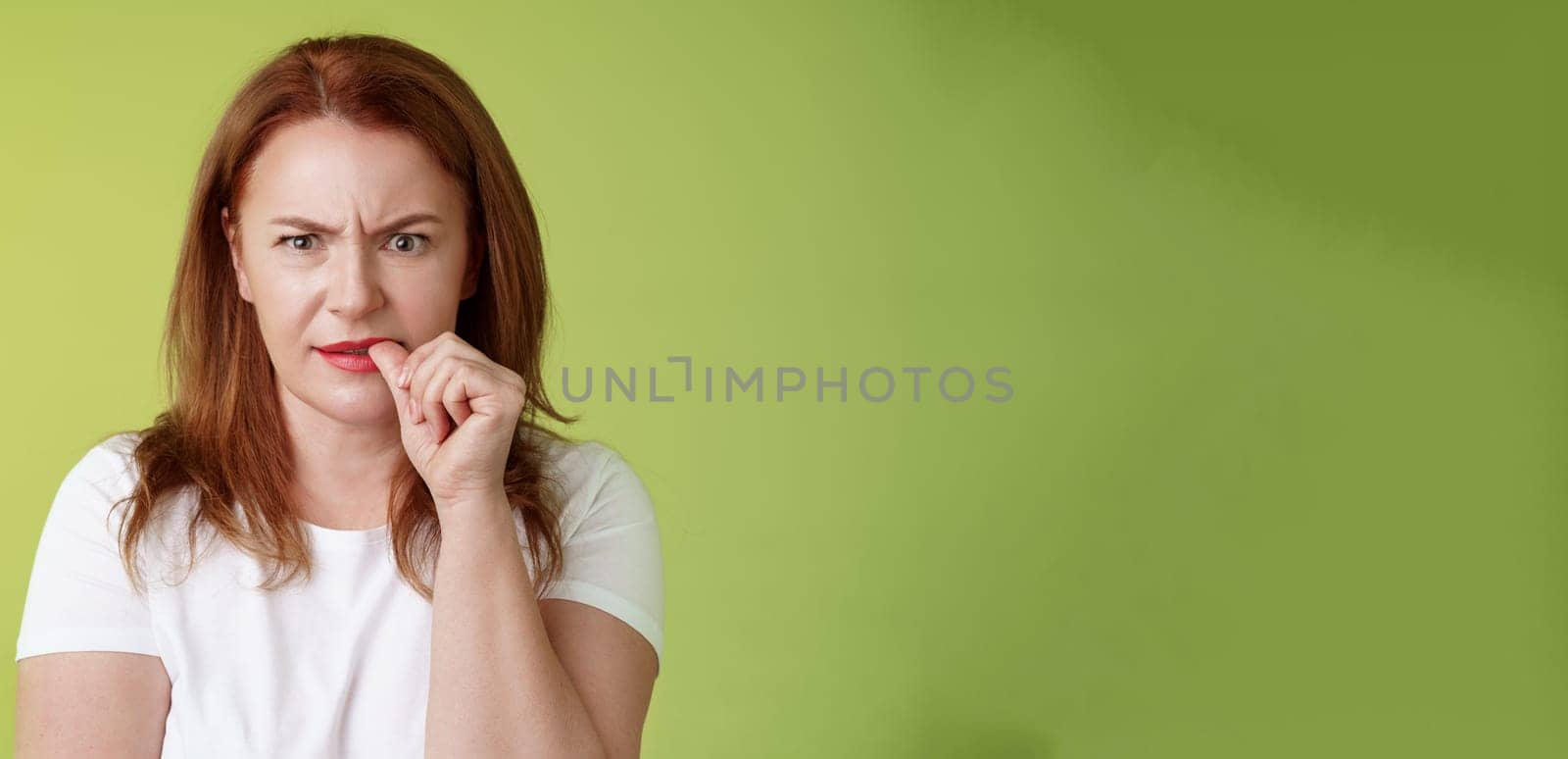Confused puzzled redhead middle-aged mother perplexed look troubled solving troublesome situation pondering solution biting thumb nail frowning intense stare camera thinking thoughtfully.