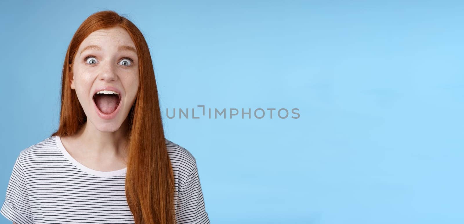 Amused thrilled enthusiastic surprised good-looking redhead girl wide eyes stunned drop jaw screaming astonished look impressed excited awesome news hearing incredible rumor, blue background by Benzoix
