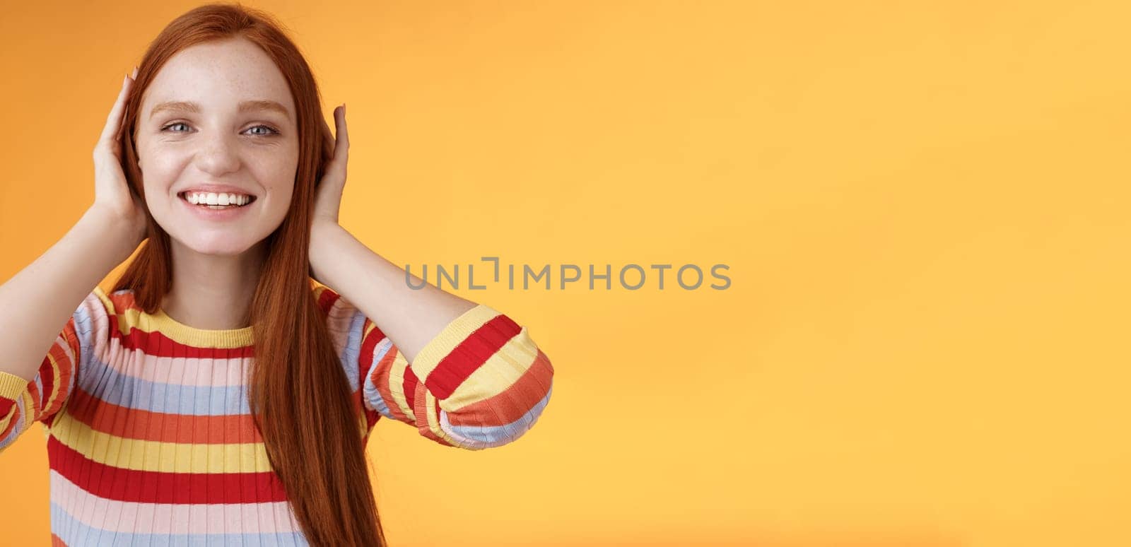 Cute playful tender smiling ginger girl blue eyes silly cover ears palms grinning fool around not hear anyone carefree unwilling listen noisy people standing careless relaxed orange background by Benzoix