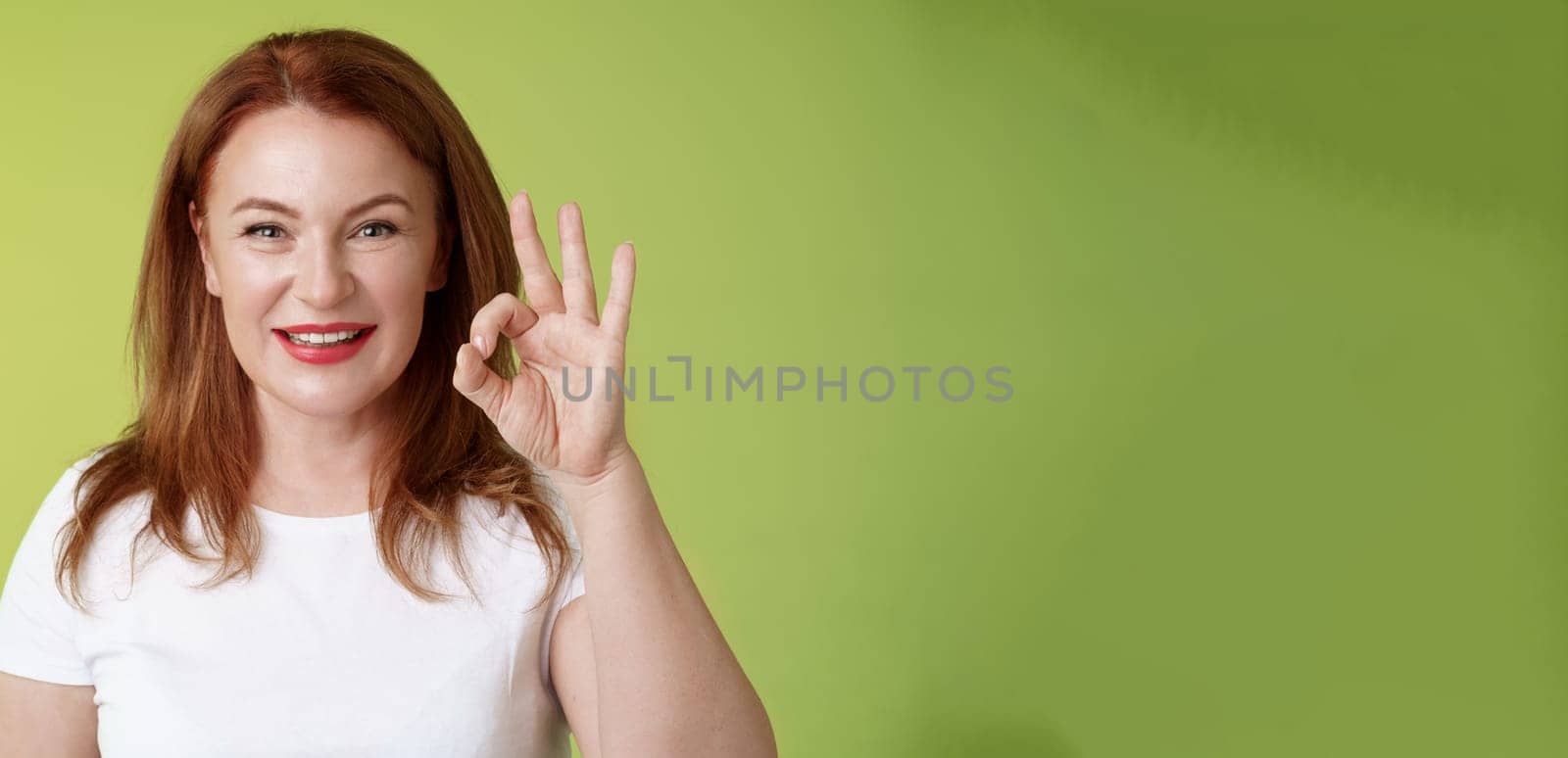 Alright got it. Cheerful motivated determined redhead enthusiastic middle-aged woman show okay ok confirm gesture assured smiling satisfactory gesture give positive like approval green background.