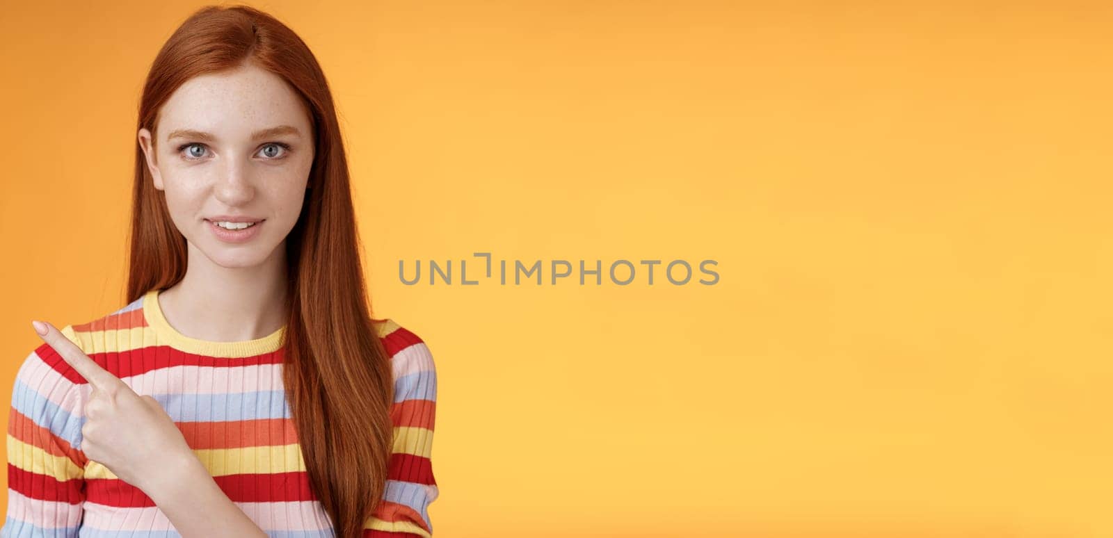 Lifestyle. Curious smart female redhead coworker asking friend who was that pointing left index finger look camera thoughtful questioned wanna know answer smiling intrigued standing orange background.