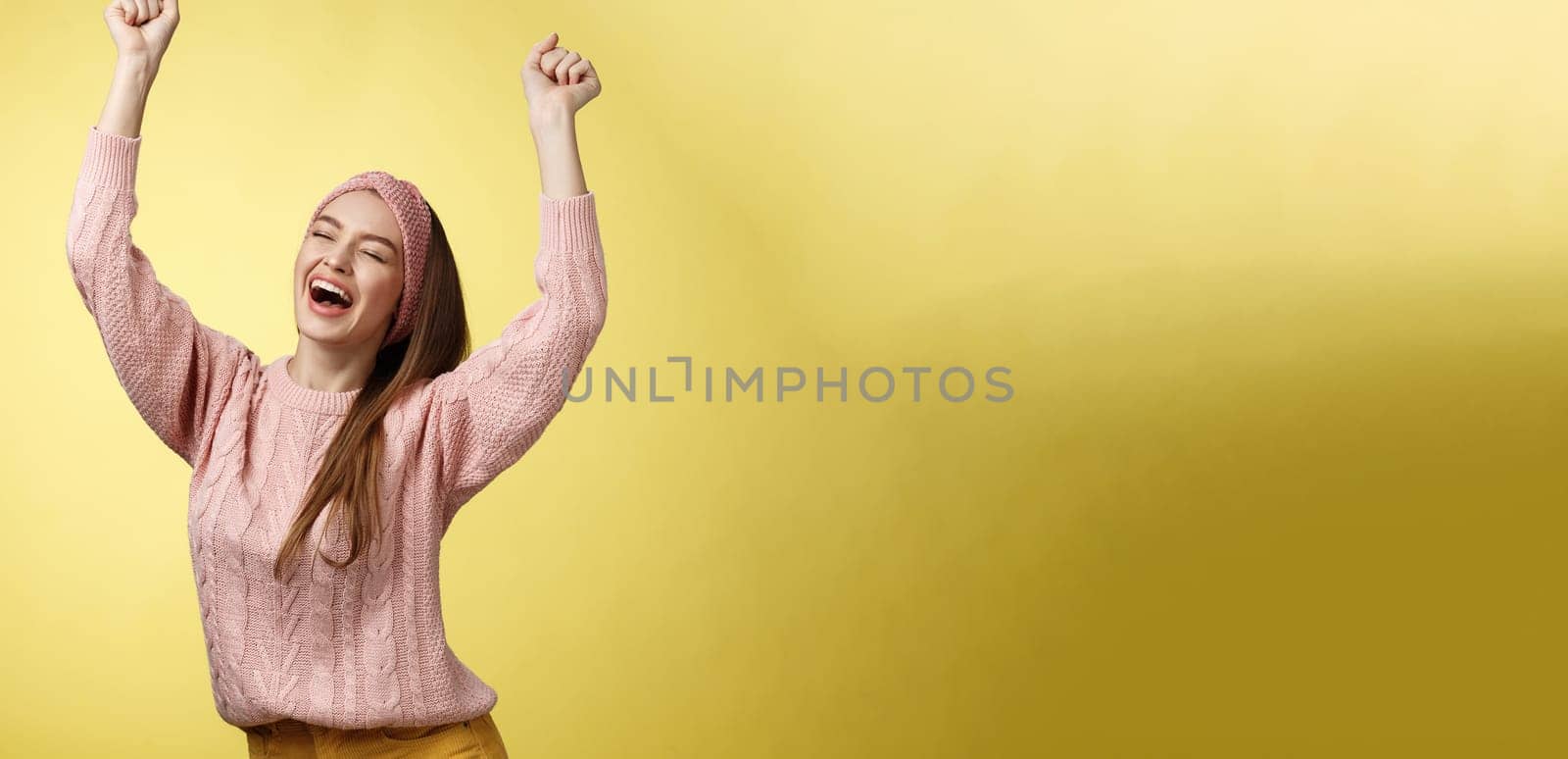 Positive celebating happy european young woman wearing casual sweater yelling happily shouting yes, triumphing racing hands up in success jumping ecstatic rejoicing cheerfully over success. Copy space