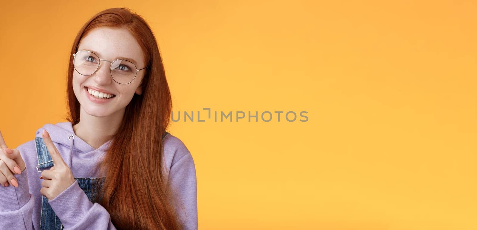 Carefree charismatic happy silly young cute redhead girl freckles blue eyes wearing glasses enjoy contemplating entertaining exhibition pointing looking left indicating, orange background by Benzoix