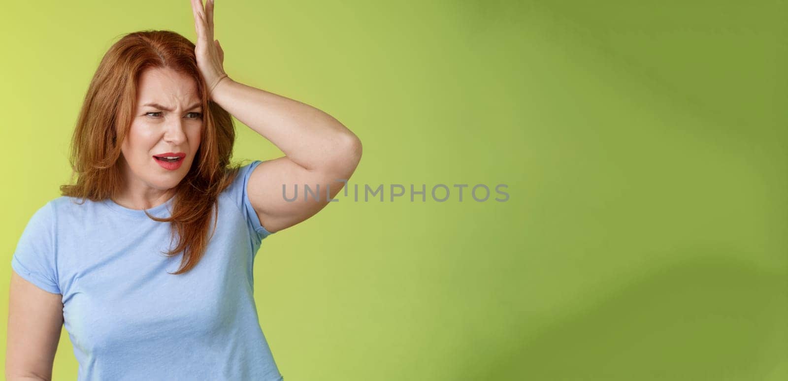 Something important slip my mind. Concerned worried upset redhead mature woman punch forehead turn away frustrated frowning disappointed forget cancel appointment stand green background by Benzoix