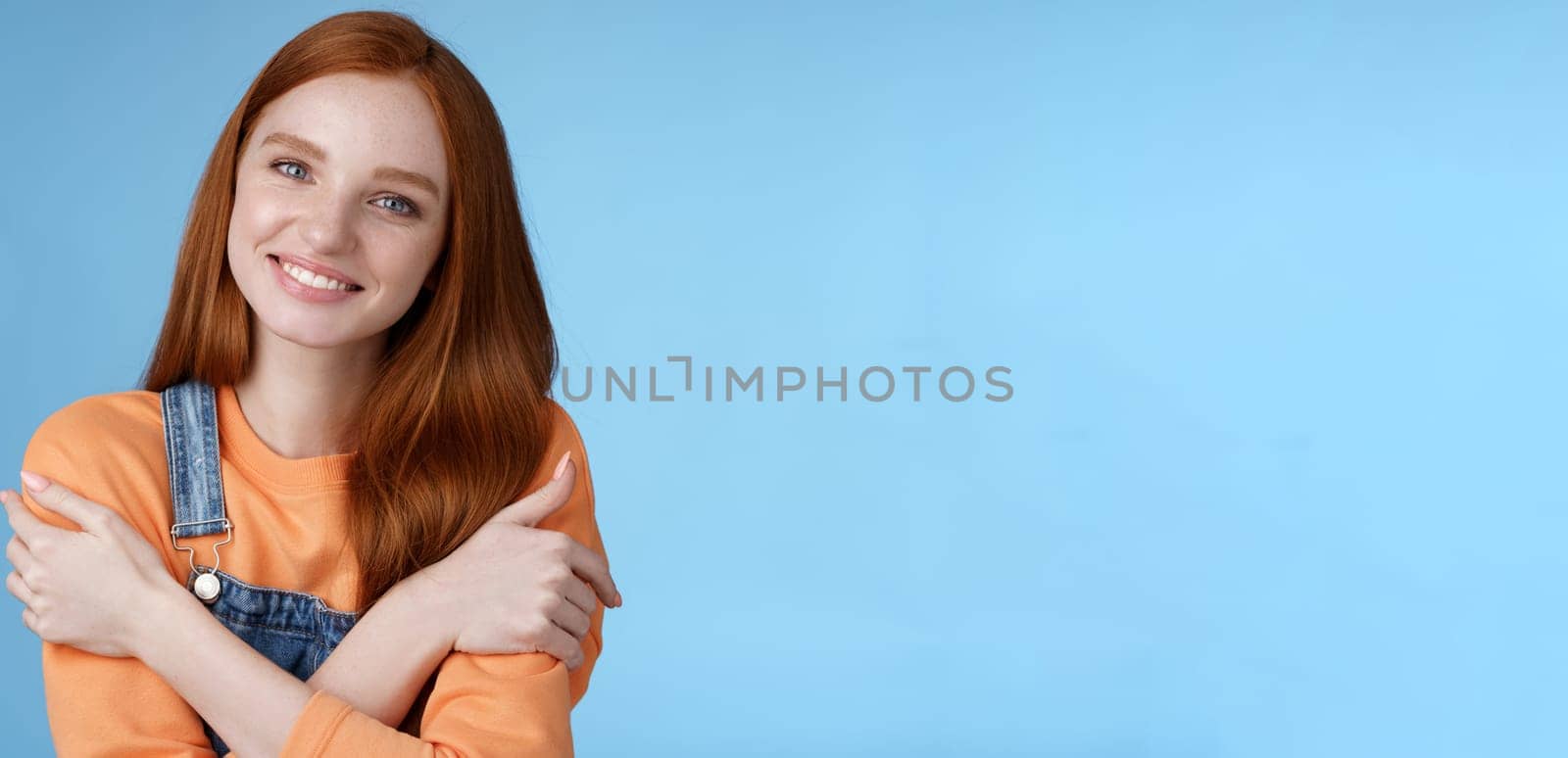 Lifestyle. Tender silly redhead girl standing blue background smiling joyfully hugging arms crossed body feel chilly grinning delighted talking boyfriend romantic date asking lend jacket cold summer evening.