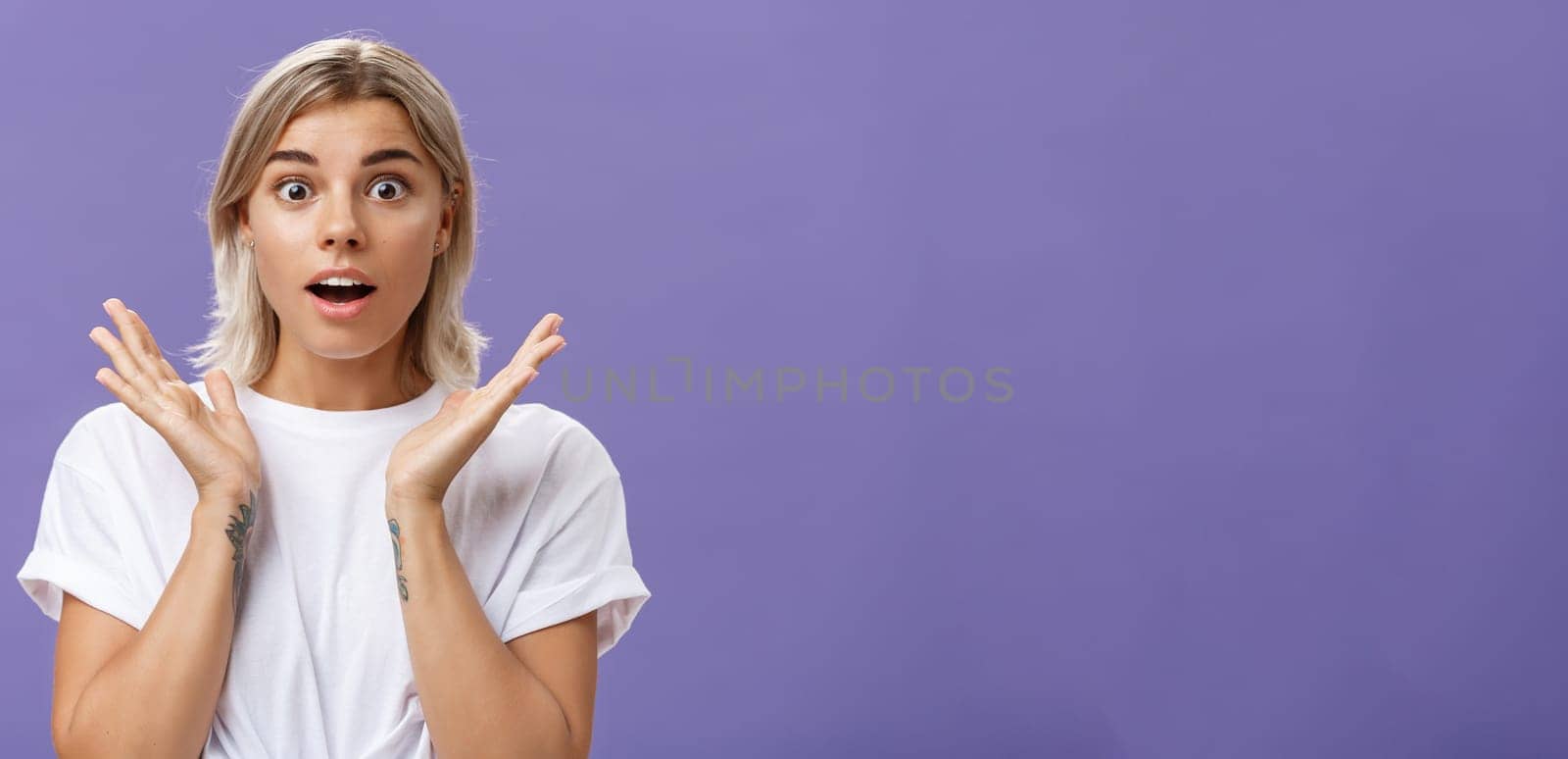 Lifestyle. Close-up shot of charmed and impressed good-looking caucasian girlfriend with blond hair and tattoos on arms raising hands in amazed and excited gesture opening mouth and gazing mesmerized at camera.