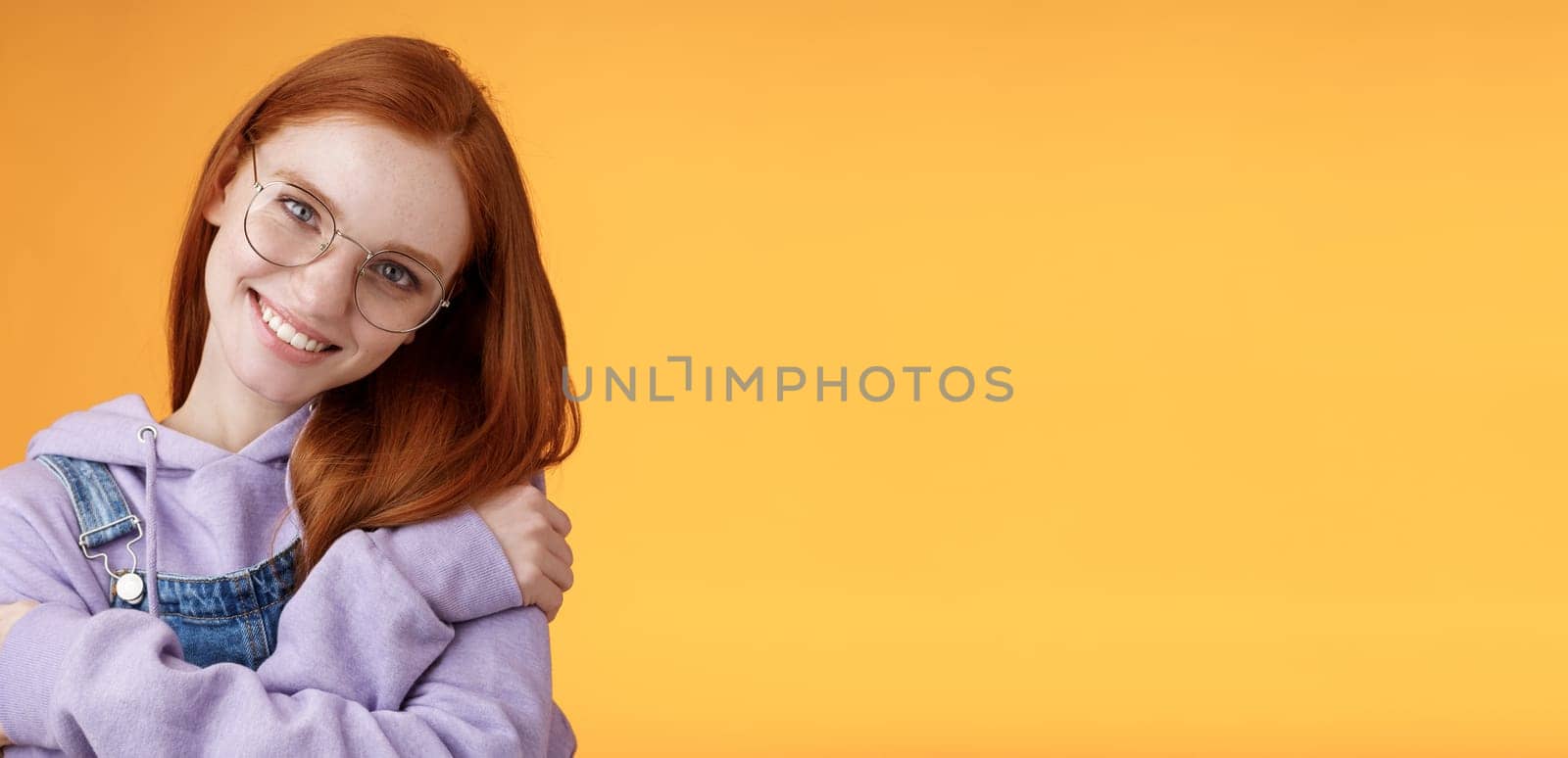 Passion, tenderness, wellbeing concept. Girl accept own self smiling charming grin tilt head hugging herself embracing body feel happiness delighted relaxing, flirty gaze camera orange background.