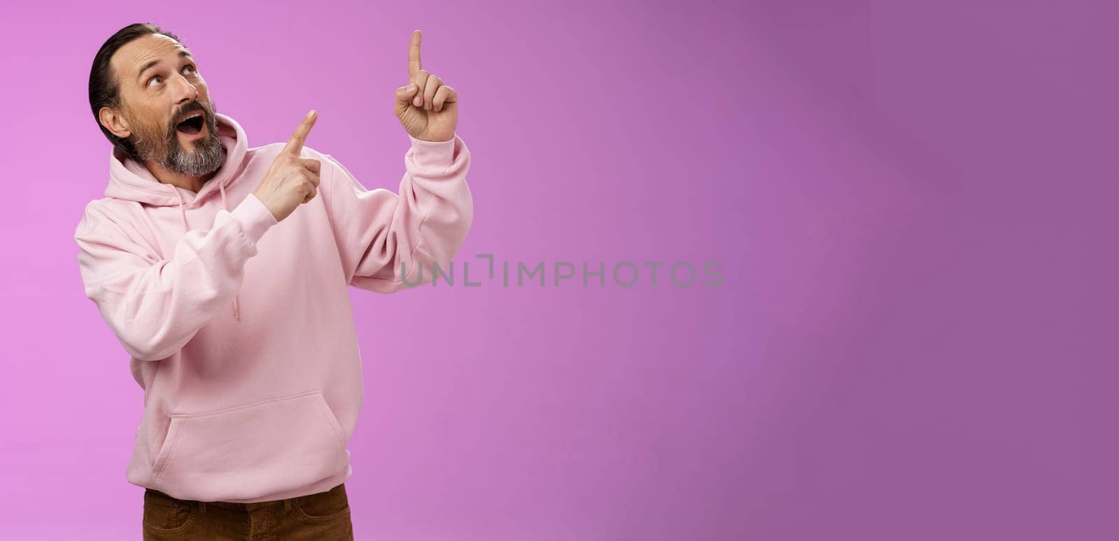 Enthusiastic energized charismatic grandfather bearded grey hair in hipster modern hoodie pointing looking impressed fascinated upper right corner discussing interesting fashion trends by Benzoix