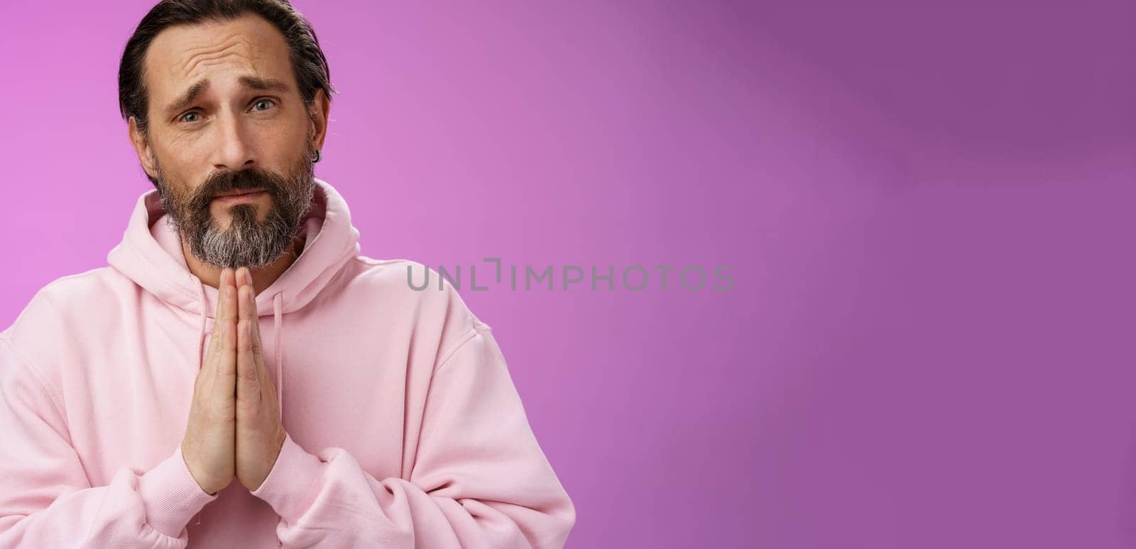 Upset handsome bearded mature man need help asking forgiveness supplicating press palms together praying frowning sorrow begging favour lend money, standing purple background miserable by Benzoix