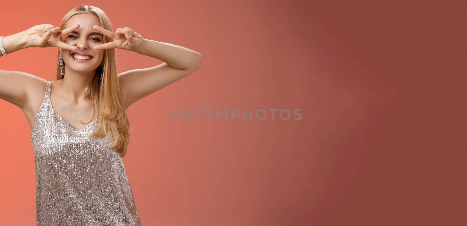 Sassy attractive stylish european girlfriend having fun celebrating birthday standing silver evening glittering dress winking cheeky make disco peace gesture near eyes enjoying party, red background by Benzoix