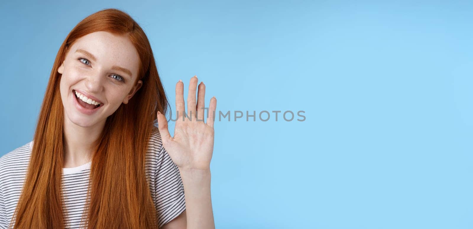 Attractive confident redhead sassy girl pure clean skin blue eyes tilting head cheerfully waving hand hello hi gesture greeting you look camera friendly welcoming friend, standing studio background.