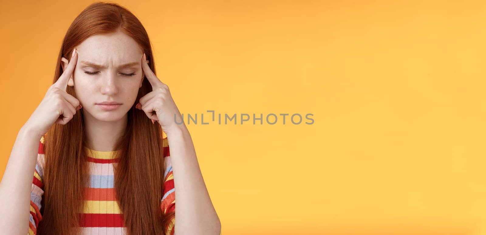 Girl getting thoughts piled trying think stright focusing concentrating important task remember number touch temples close eyes look seriously standing puzzled suffer headache, orange background.