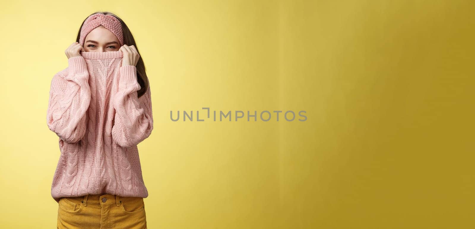 Cute playful young girl hiding in sweater peeking and squinting flirty over top of cloth pulling collar on nose, fooling around having fun happily, being in positive good mood, warming-up on cold day by Benzoix