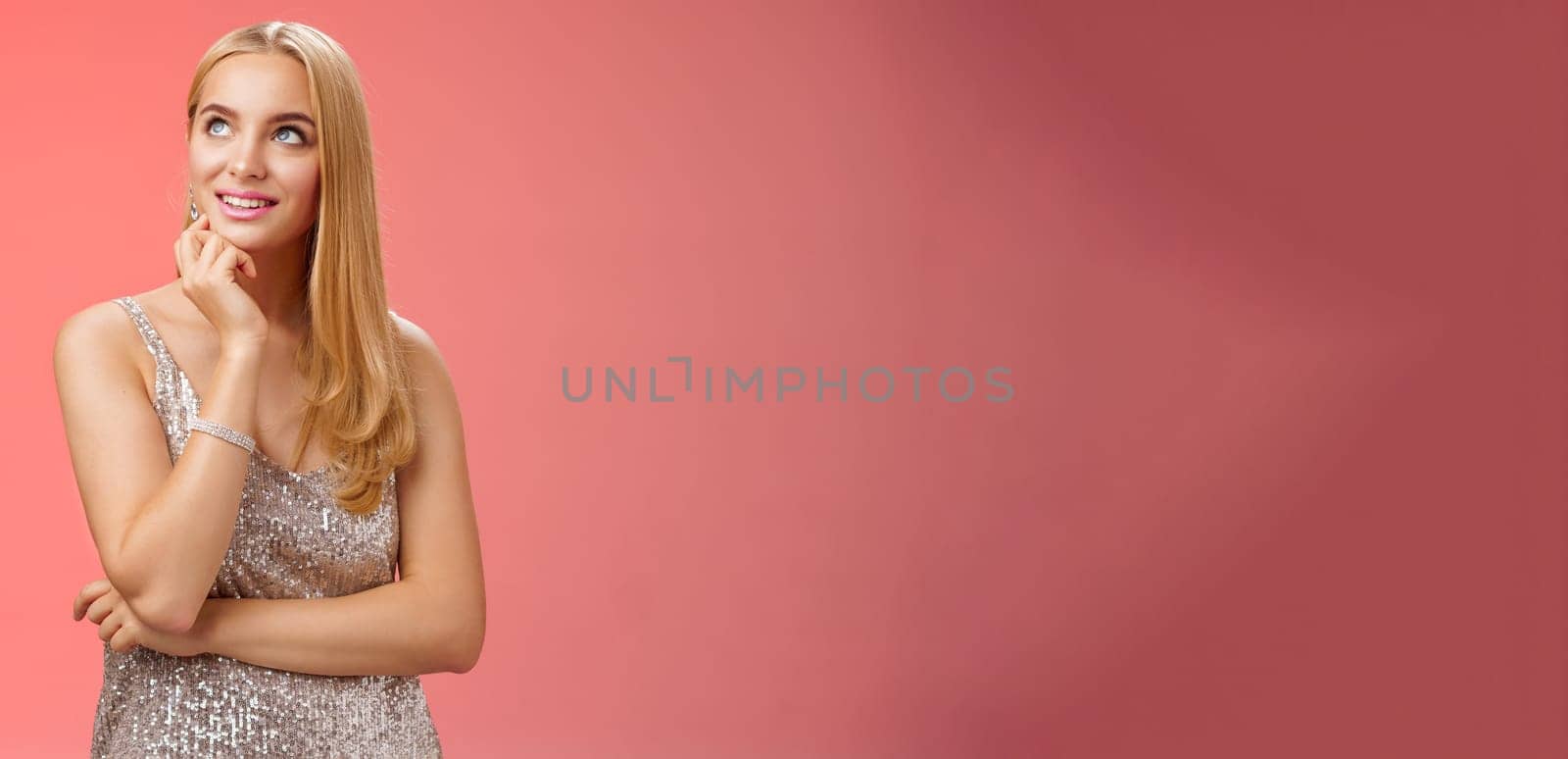 Lifestyle. Dreamy charming elegant blond young woman in silver glittering evening dress look up thoughtful enjoying fashion week afterparty standing casually relaxed red background thinking planning mind.