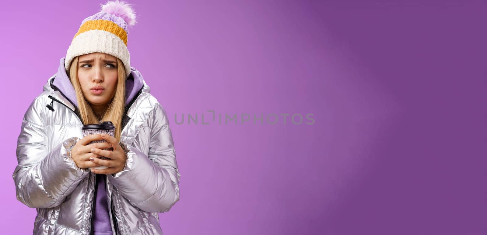 Trembling uncomfortable cute pouting young blond girl feel freezing cold winter snowy weather outside shaking low temperature hold take-away hot coffee cup warming up, purple background by Benzoix