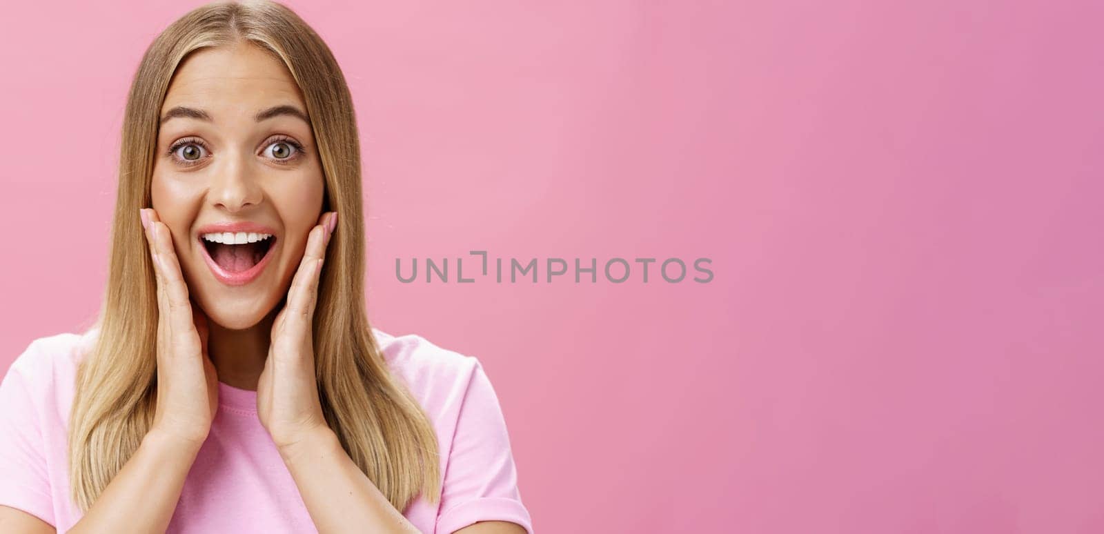 Woman surprised to see own face without imperfactions treating acne feeling beautiful and happy touching cheeks, smiling amazed, joyful looking with admiration and excitement at camera over pink wall by Benzoix