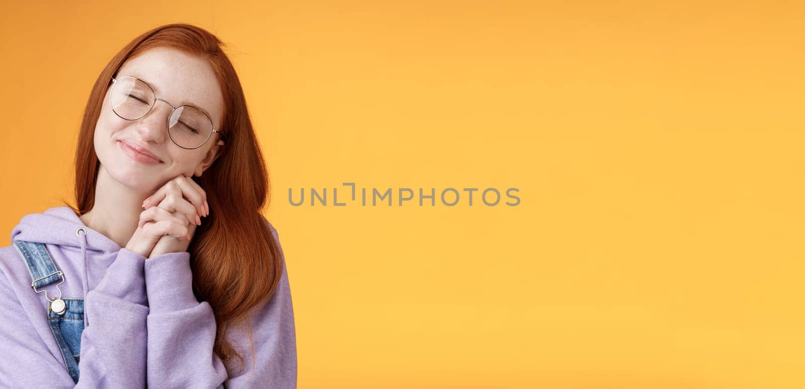 Sweet tender happy romantic redhead girlfriend close eyes smiling dreamy imaging lovely scene daydreaming press palms cheeks silly recalling nice memories, standing orange background relaxed.