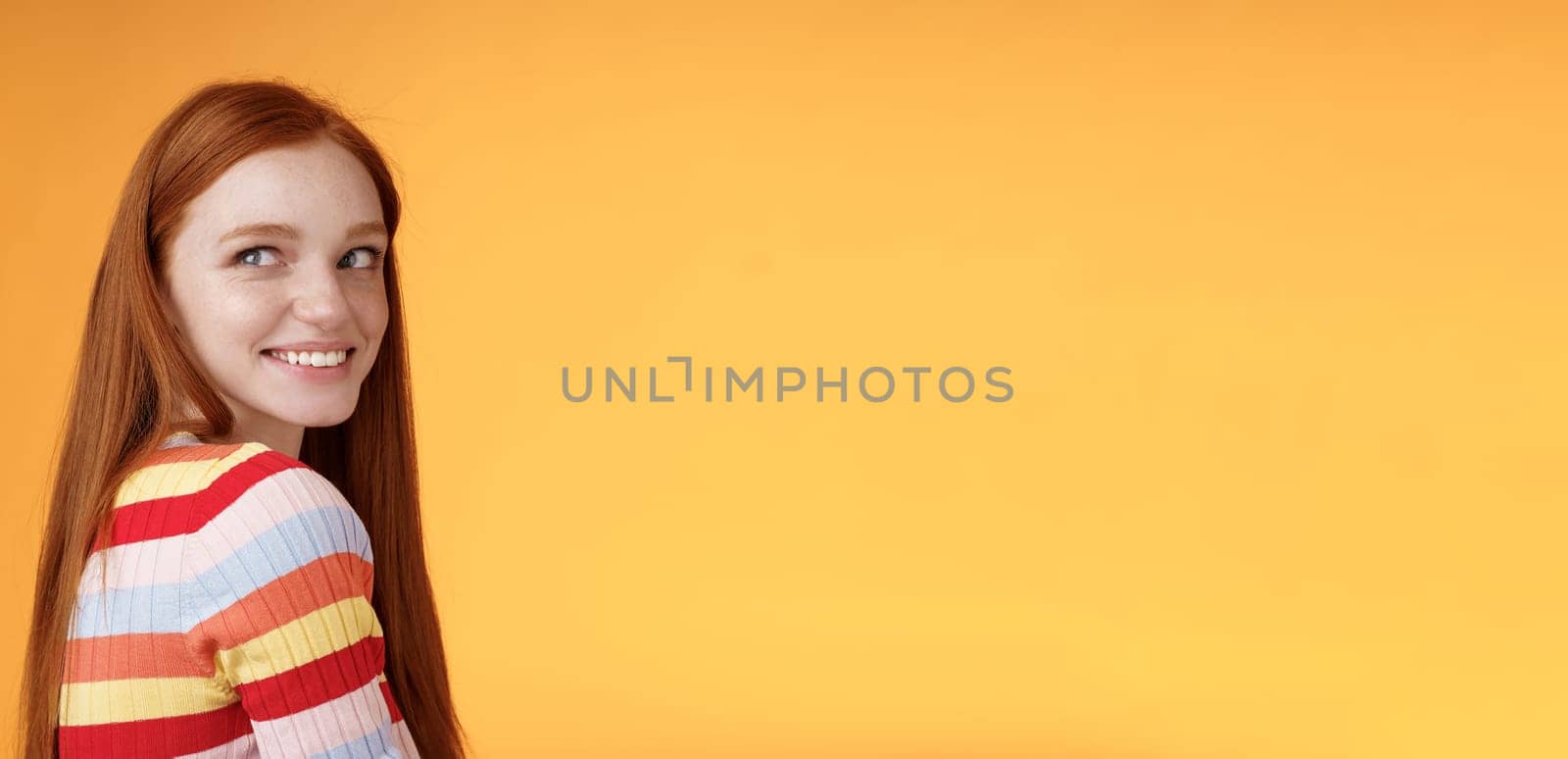 Tender romantic carefree european redhead girlfriend turning behind look left amused smiling pleased coquettish gaze standing orange background flirty romantic mood wanna receive date invitation by Benzoix