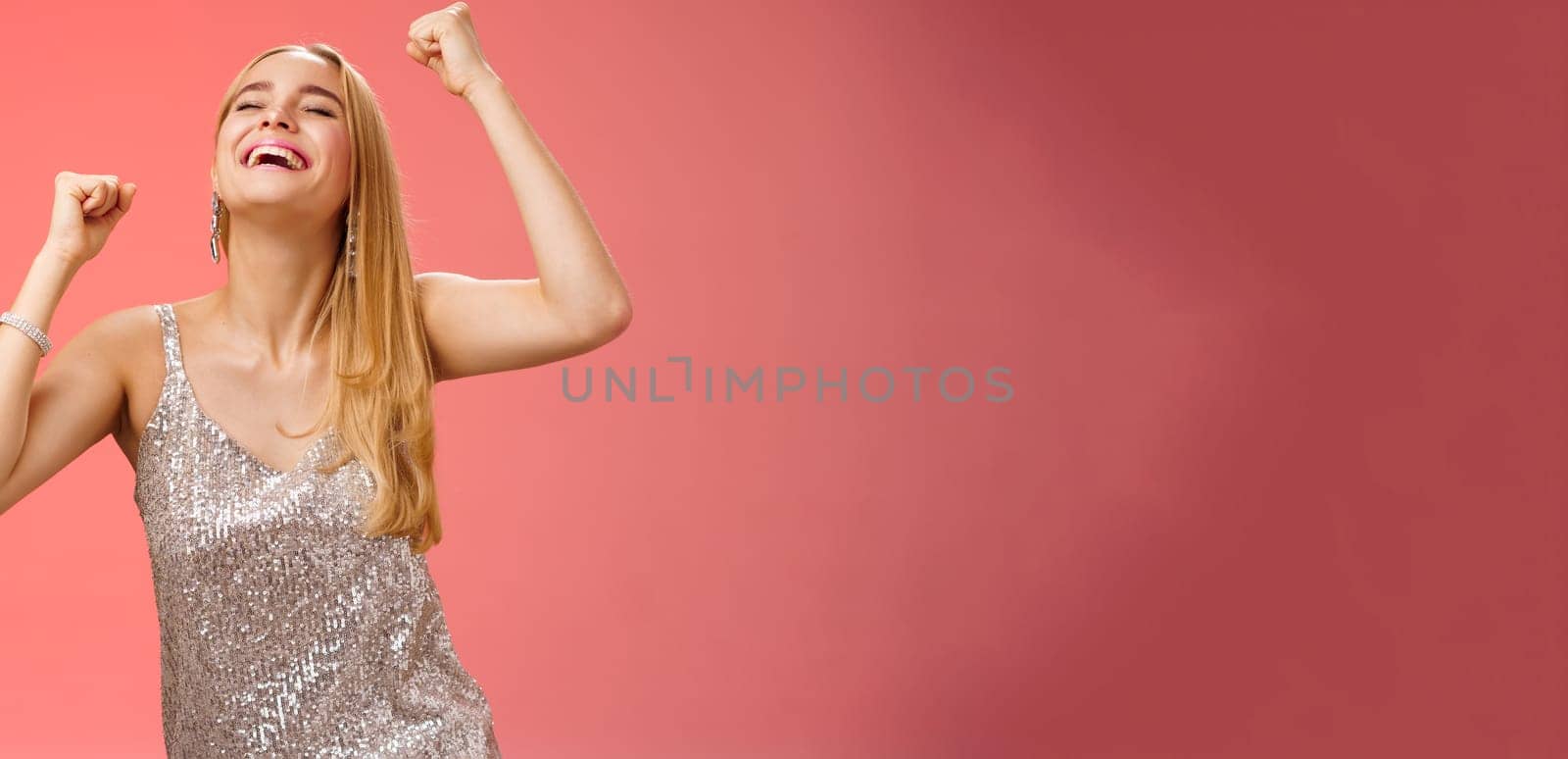 Excited carefree happy stylish blond european woman having fun dancing smiling broadly laughing happiness enjoying awesome music party rocking lighting dance-floor standing red background by Benzoix