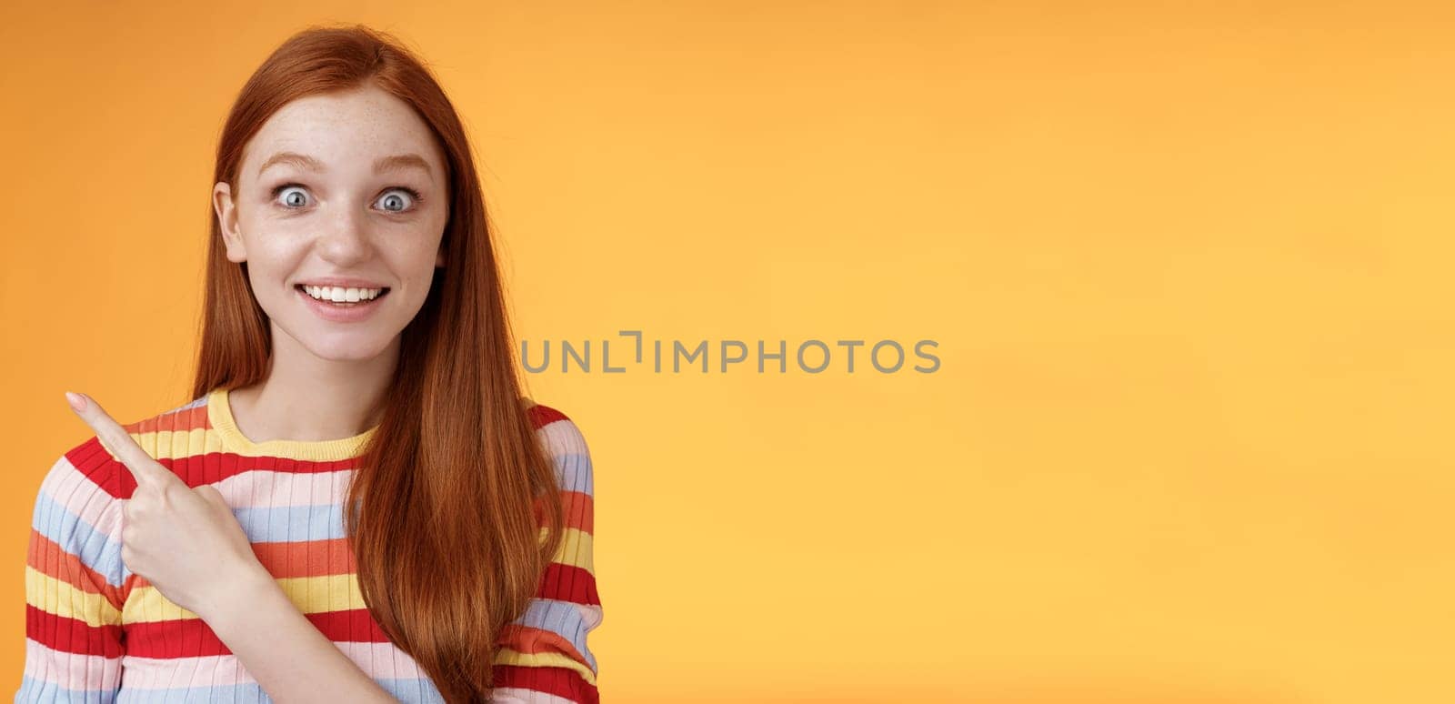 Excited thrilled good-looking young silly redhead girl surprised pop eyes camera gasping impressed pointing upper left corner see super star grinning excitement delight, orange background by Benzoix