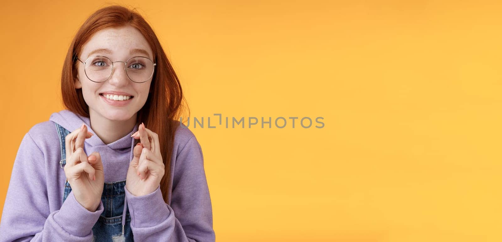 Hopeful young cute silly dreamy redhead attractive girl ginger straight haircut wearing glasses begging lord help cross fingers good luck desire win dream come true praying wish fulfill. Lifestyle.