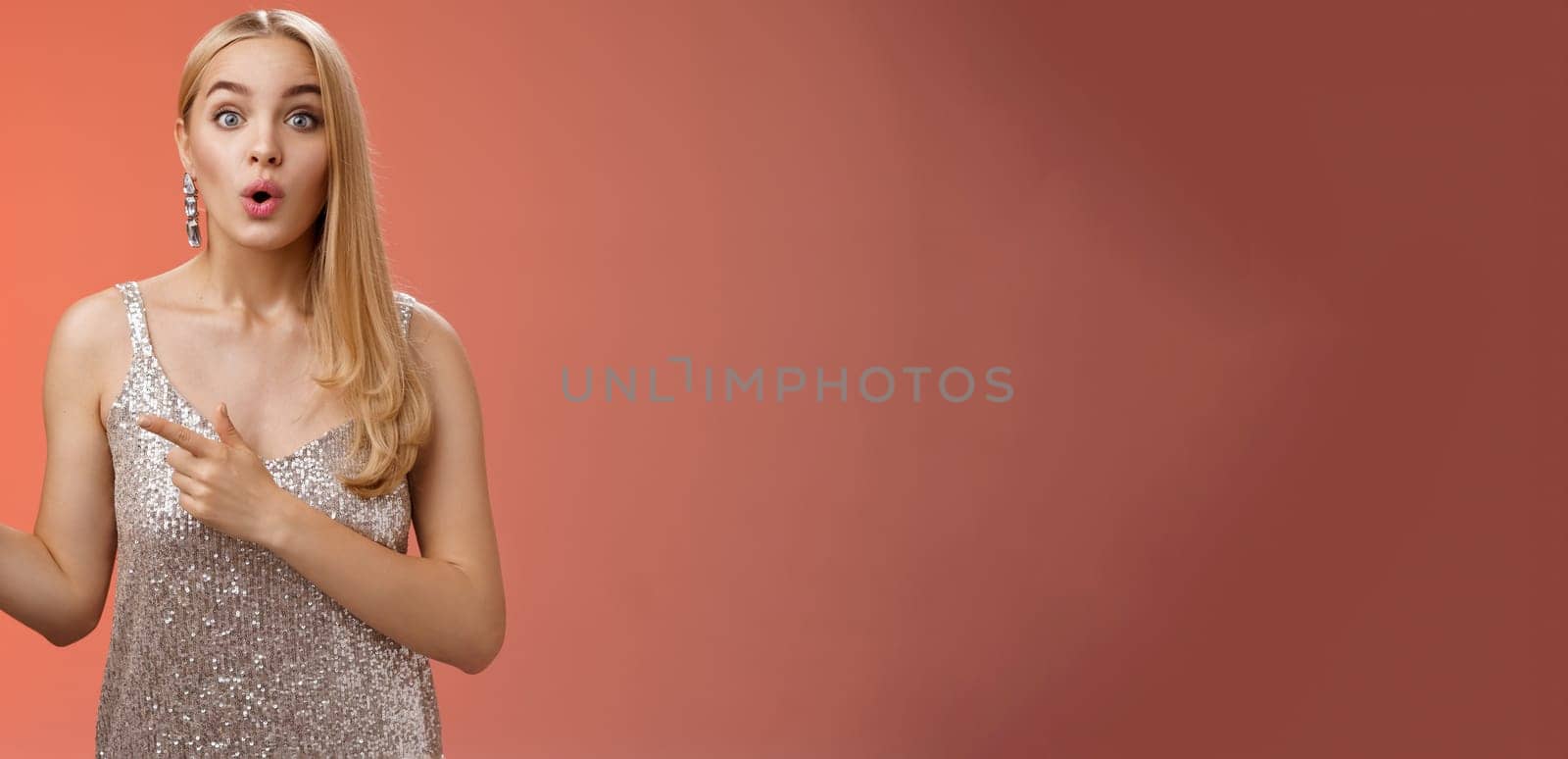 Intrigued excited attractive tender feminine blond european girl in silver stylish dress pointing left amused talking camera widen eyes thrilled asking boyfriend wanna dance shall go check out promo by Benzoix