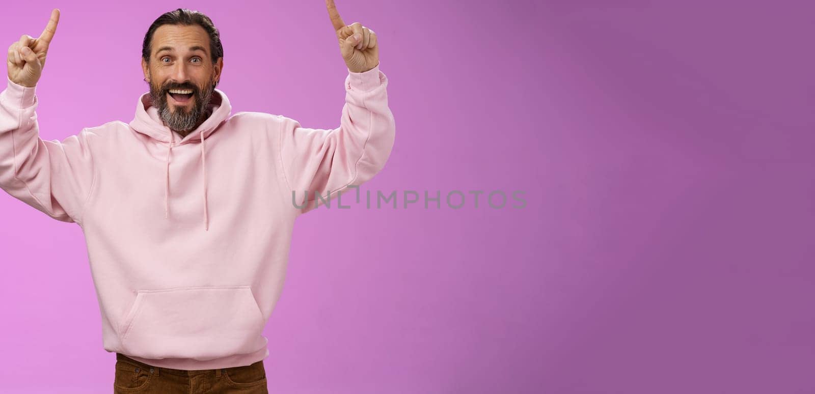 Lucky carefree stylish mature man beard grey hair raising hands joyfully pointing up introduce cool place trying stay young soul wanna hang together grandchildren, standing purple background by Benzoix