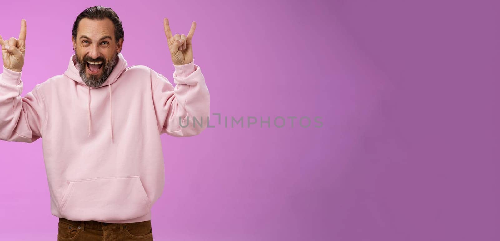 Carefree enthusiastic excited mature bearded man grey hair having fun show rock-n-roll gesture attend awesome heavy metal concert grimacing thrilled looking happy upbeat, purple background.