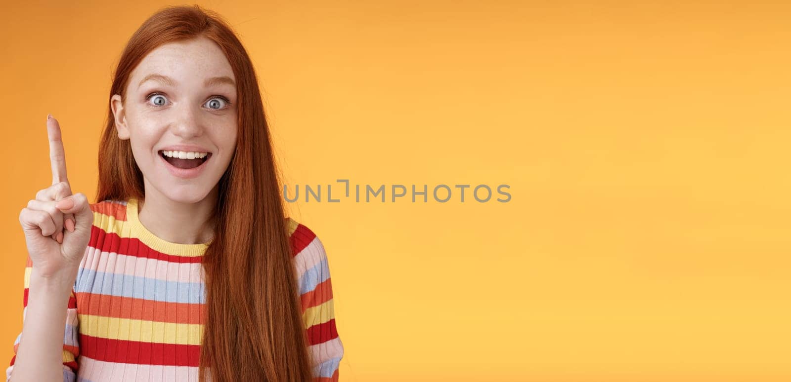 Excited happy cheerful young redhead female student got idea think answer raising index finger eureka gesture smiling thrilled wide eyes saying plan have excellent suggestion, orange background.