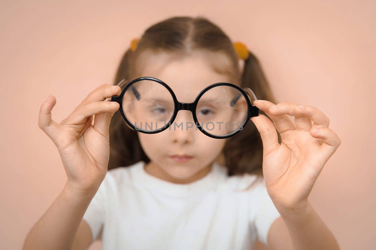 Portrait of an out-of-focus smart preschool girl holding round diopter glasses in front of her in focus.