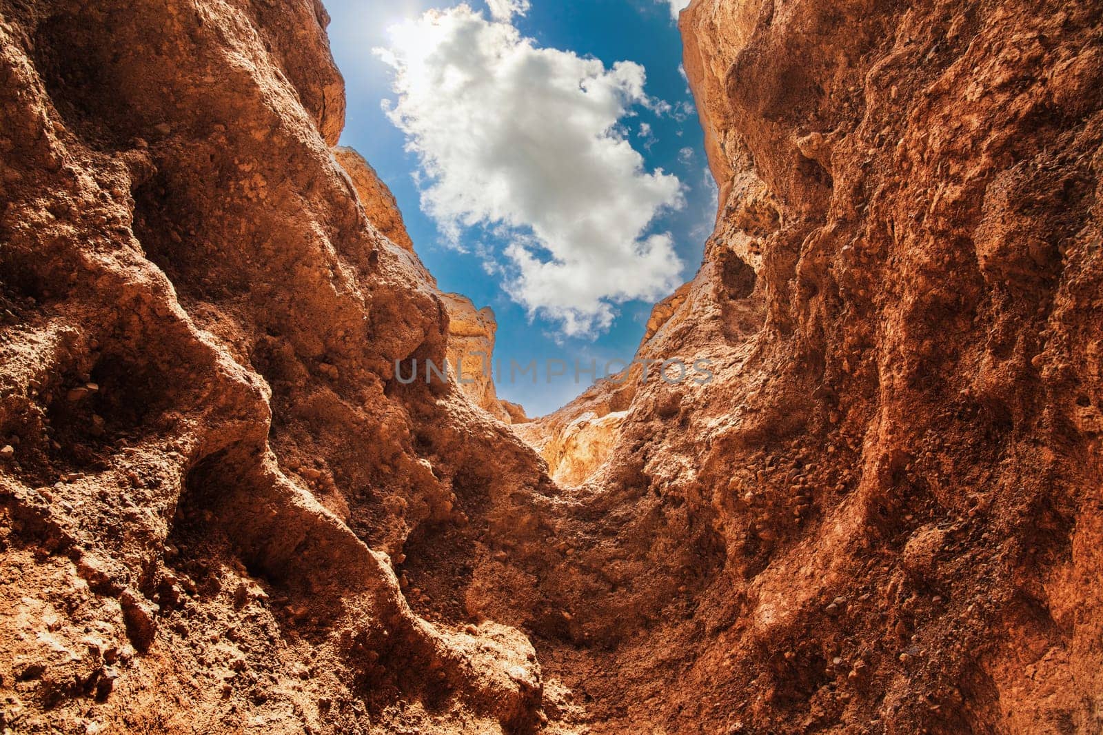 Red rock walls of Charyn canyon and piece of blue sky with fluffy cloud in the national park of the Almaty region. Picturesque nature of South-Eastern Kazakhstan.
