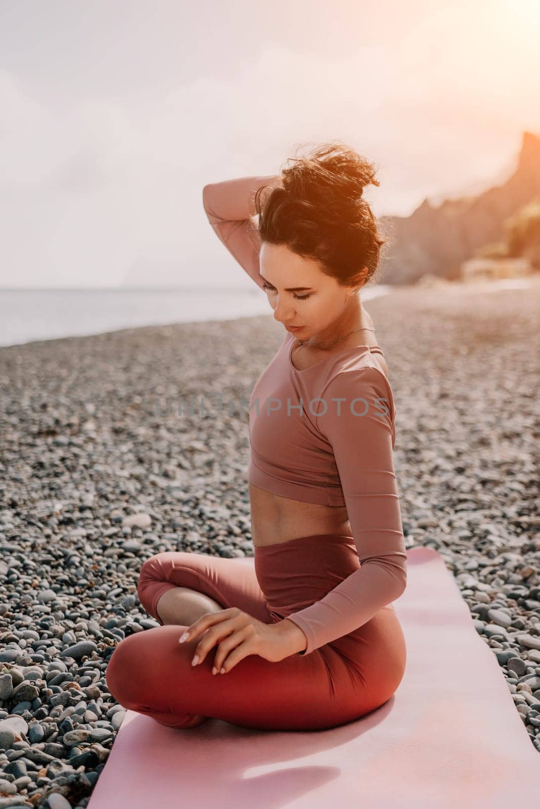 Middle aged well looking woman with black hair, fitness instructor in leggings and tops doing stretching and pilates on yoga mat near the sea. Female fitness yoga routine concept. Healthy lifestyle by panophotograph