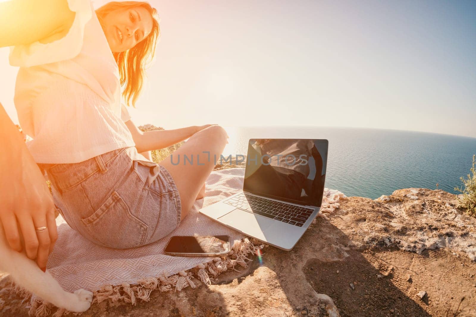 Woman sea laptop. Business woman petting cat and working on laptop by the sea. Close up on hands of pretty lady typing on computer outdoors summer day. Freelance, digital nomad and holidays concept. by panophotograph