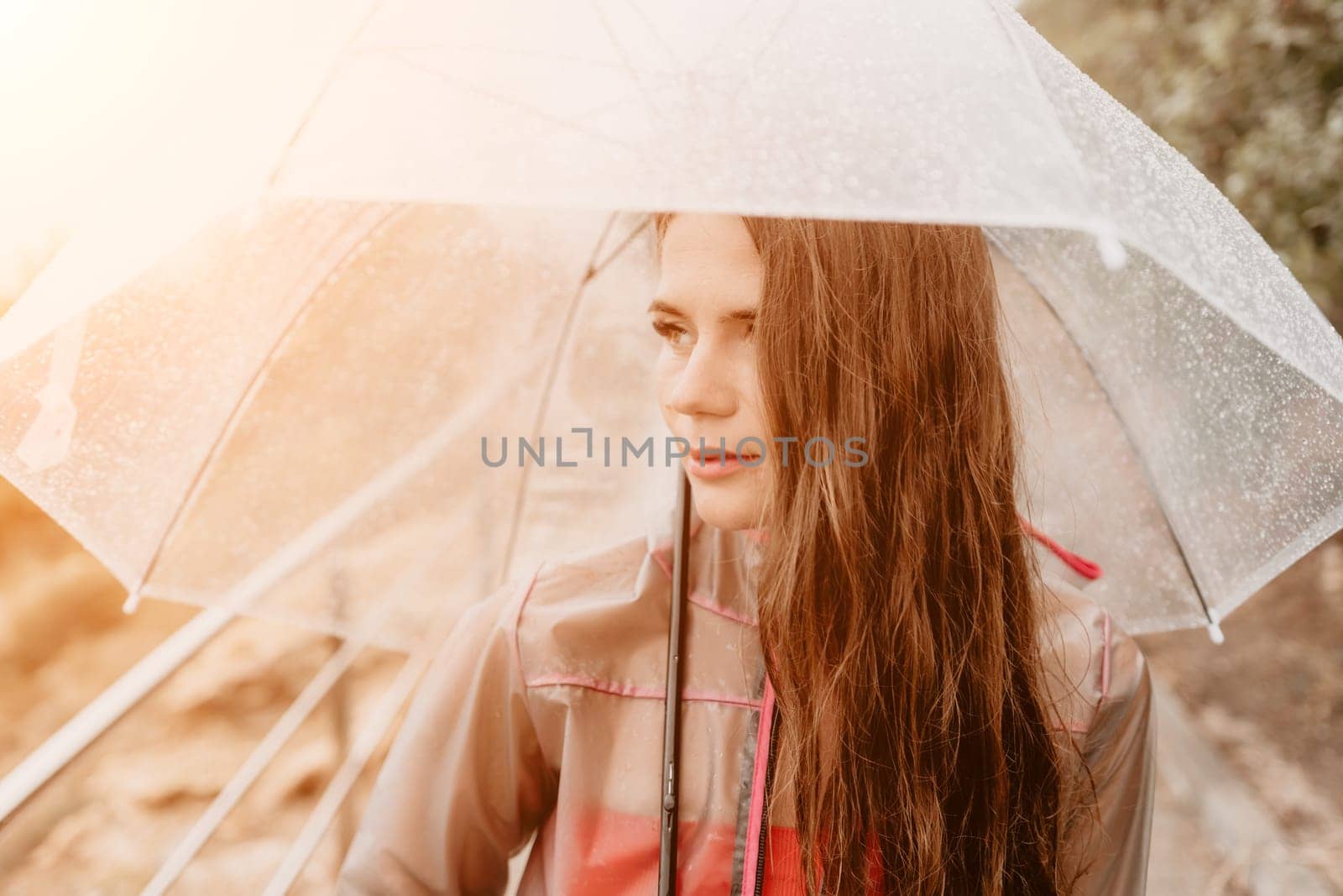 Woman rain umbrella. Happy woman portrait wearing a raincoat with transparent umbrella outdoors on rainy day in park near sea. Girl on the nature on rainy overcast day. by panophotograph