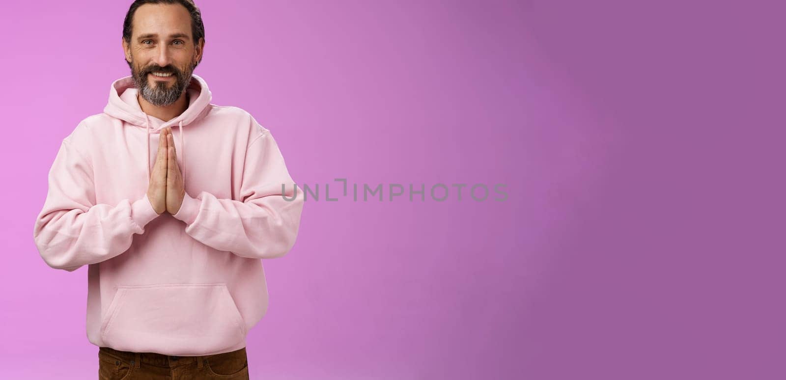 Peaceful attractive bearded mature mail model in trendy pink hoodie press palms together namaste praying gesture smiling delighted relaxed bowing buddhism faith, appreciating help, look thankful.