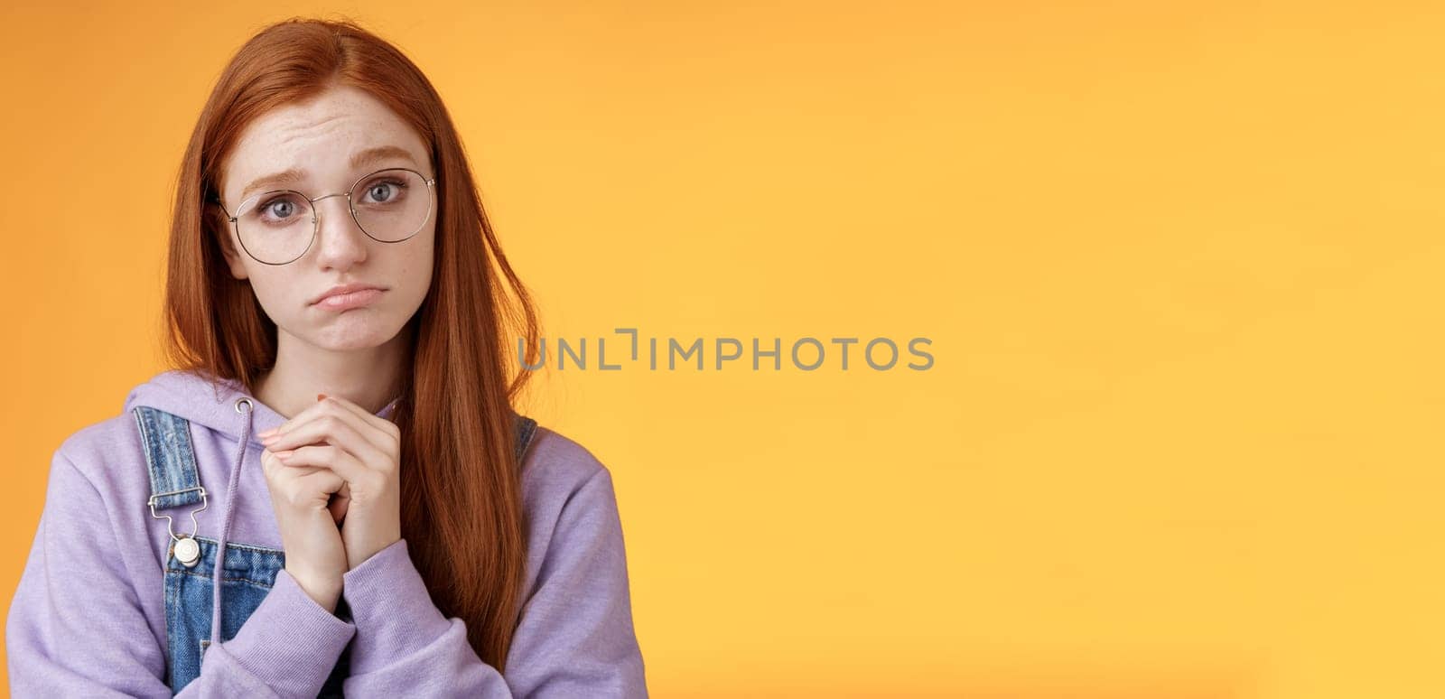 Pretty please. Clingy young sad sulking redhead girl sibling wearing glasses pouting silly press palms begging gesture pleading wanna receive help promise be good ask favour, orange background.