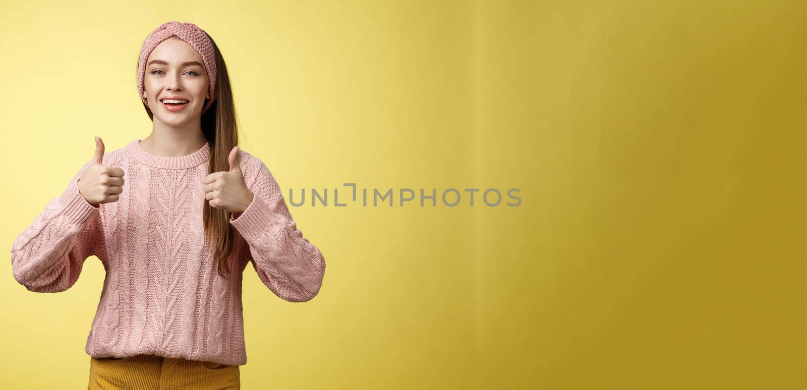 Attractive positive young girl in knitted sweater agree with suggestion, approving plan, showing thumbs up, recommending awesome film, smiling, cheering, supporting friend effort, encouraging.